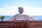 Rear view of senior man  sitting in a bench at sea, looking at horizon over water. Relaxed elderly enjoying retirement