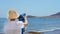 Rear view of senior woman traveler wearing hat and holding blue telescope binocular adjusting lens