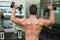 Rear view of shirtless muscular man exercising with dumbbells