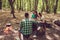 Rear view shot of guy playing guitar in the wood near fire. Three friends are sitting near, smiling, enjoying. Dinner is cooking