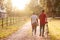 Rear View Shot Of Romantic Couple Walking And Pushing Bike Along Country Lane At Sunset