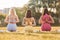 Rear view. Sitting in lotus pose with hands on the back. Group of women have fitness outdoors on the field together