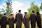 Rear view of six successful international young graduates in black robes and hats finished their education, holding hands and