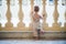 A rear view of small toddler girl looking through concrete railing on summer holiday.