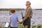 Rear View On Smiling Grandfather And Grandson Going To Fish On Riverside in Countryside