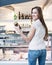 Rear view of smiling woman holding chocolate jar in front of display cabinet at cafe