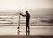 Rear view of strong surfer with surfboard on the beach at sunset or sunrise. Silhouette of surf man standing looking at ocean