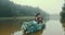 Rear view of the stylish couple in vintage sloth floating on romantic boat decorated with green herbs along the foggy