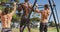 Rear view of three diverse shirtless fit men exercising outside, doing chin-ups on a climbing frame