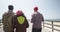 Rear view of three ethnic hipster friends walking down pier at the beach