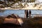 Rear view of three tourist girls standing on lake shore in front of tent enjoying beautiful sunset