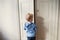 A rear view of toddler boy standing near door inside in a bedroom.