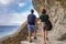 Rear view of tourists man and woman walking on stony trail at sea shore. Couple with backpacks travelling and discovering places