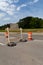 Rear view of traffic barricade and safety barrels, asphalt roadway copy space, blue sky and trees