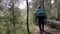 Rear view of traveler walking down forest path. Stock footage. Traveler with backpack and in raincoat goes on bumpy path