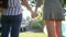 Rear view of two unrecognizable girls holding hands with LGBT bracelet in backlight stand in park