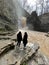 Rear view of two women looking on powerful muddy waterfall. Tourists standing on rocks in mountainous terrain and