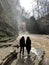 Rear view of two women looking on powerful muddy waterfall. Tourists standing on rocks in mountainous terrain and