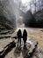 Rear view of two women looking on powerful muddy waterfall. Tourists standing on rocks in mountainous terrain and