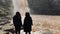 Rear view of two women looking on powerful muddy waterfall. Tourists standing on rocks in mountainous terrain and