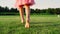 Rear view of unrecognizable girl running barefoot on green grass at city park.