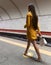 Rear view of a walking on subway platform beautiful young girl with long beautiful legs wearing a yellow spring coat and