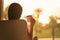 Rear view of woman with cup of coffee sitting on chair near window and looking on palm trees sea beach at sunrise. Female relaxing