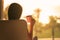 Rear view of woman with cup of tea sitting on chair near panoramic window and looking on palm trees sea beach at sunset. Female