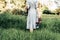 Rear view of a woman in a dress walking along a meadow barefoot with shoes in her hand