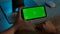 Rear view of woman holding Chroma Key green screen of smartphone in horizontal position. She scrolls through content by