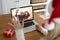 Rear view of woman in santa hat waving while having a videocall with couple in santa hats toasting o