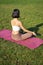 Rear view of woman silhouette doing yoga, sitting on fitness mat and meditating on green lawn