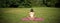 Rear view of woman silhouette doing yoga, sitting on fitness mat and meditating on green lawn