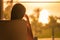 Rear view of woman sitting on chair near window and looking on palm trees sea beach at sunrise. Female relaxing.