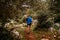 rear view of woman with trekking poles walking along path along bushes and stones