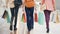 Rear view of women`s legs in jeans walking in shopping mall, girls are carrying bright paper bags with purchases