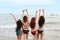 Rear view of young asian beautiful and joyful girls in bikini who dancing and raising hands on tropical beach with happy and smile