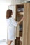 Rear view young cheerful caucasian woman in white pajama choosing clothes in wardrobe in bedroom with happy face life style and