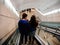 Rear view of young couple descending on escalator to change the train platform