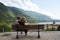 Rear view of a young couple sitting and hugging on a Bench in front of the mountain lake. The man is embracing her girlfriend