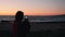 Rear view of young female standing on beach and making photos and videos of sea sunset. Woman takes pictures of beautiful sundown.