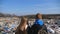 Rear view of young girl and boy stands against the blurred background of dirty garbage dump. Little children looks at