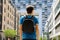 Rear view of a young man with backpack just arrived in a big city and looking to modern buildings with perspectives and