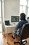 Rear view of young man, software developer writing code on desktop computer while sitting at his workplace and working