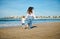 Rear view of a young mother and daughter holding hands, running barefoot, leaving footsteps on the wet sand