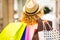 Rear view of a young  woman with blond and curly hair walking into the shopping mall with a lots of bags. Consumerism concept