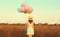 Rear view of young woman with bunch of colorful balloons wearing summer straw hat, dress in field outdoors