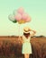 Rear view of young woman with bunch of colorful balloons wearing summer straw hat, dress in field outdoors