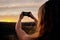 Rear view of young woman holding smartphone taking picture of morning sunrise against horizon