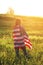 Rear view of a young woman holding the US national flag in a field at sunset. Independence Day of America. American freedom